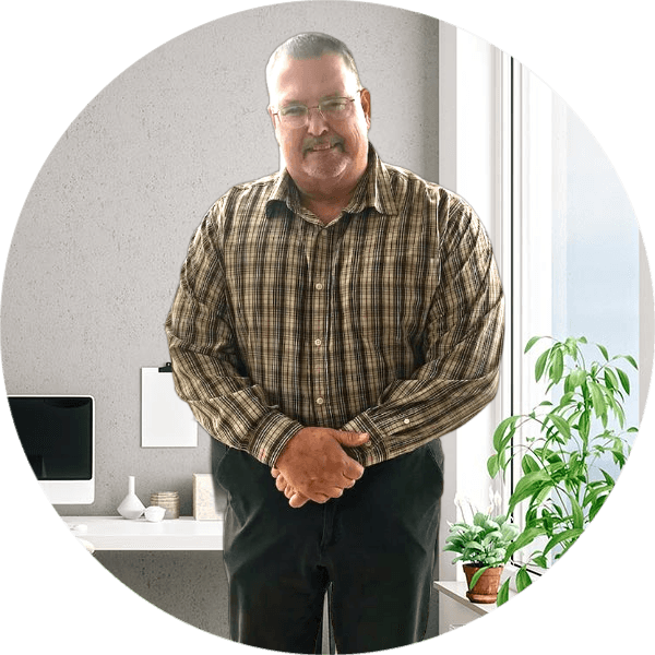 Smiling man in a plaid shirt and glasses, standing in a bright office environment.
